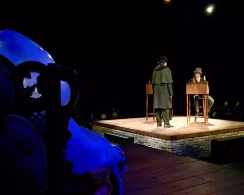 On the stage standing is Adam Kobs and sitting is Remy Garfield. The white figure sitting in the chair is Rebecca Glenister who played the ghost of Christmas past.